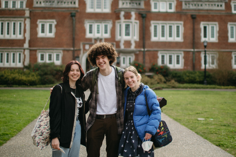 Three students stand smiling next to each other while standing infront of a Reed College residence hall.