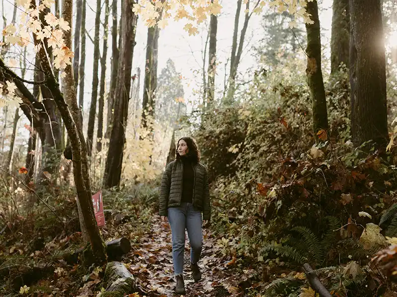 A female Reed College student walks down a forested trail covered with leaves