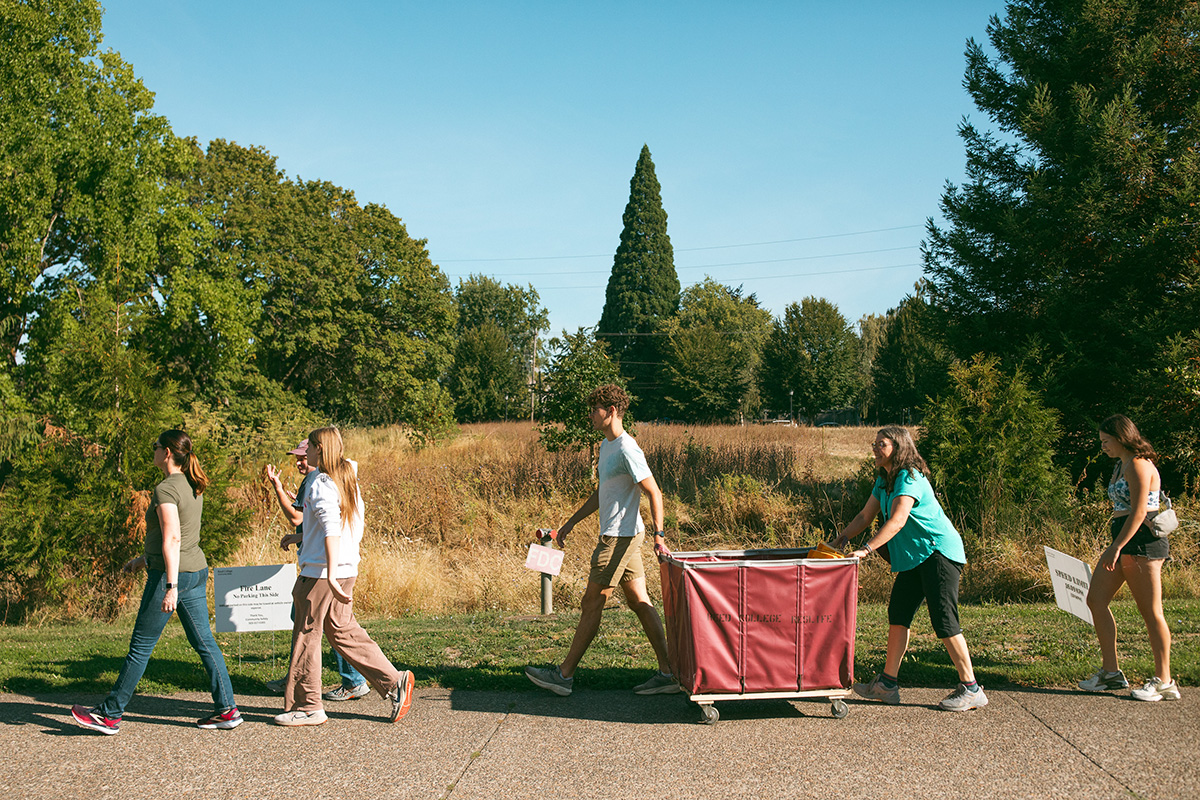 A family walking down the sidewalk towards the Reed College Apartments, the mother pushing a pushcart full of her student's belongings