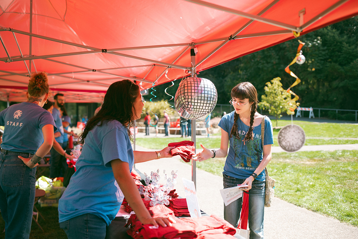 A student receiving a t-shirt from a staff member at the Orientation information table