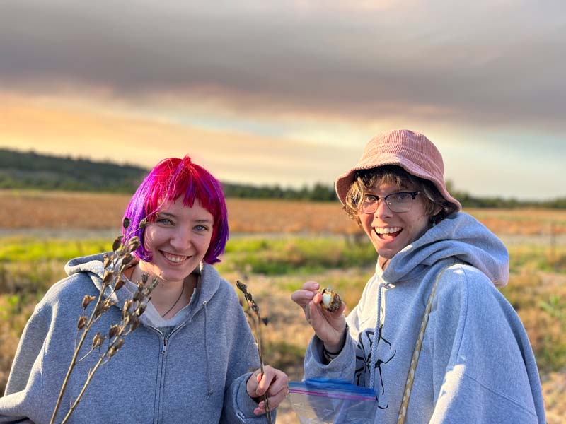 Two students wearing gray hoodies smiling and standing in a field