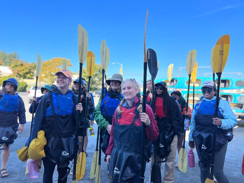 A group of students holds kayak paddles as they prepare to kayak