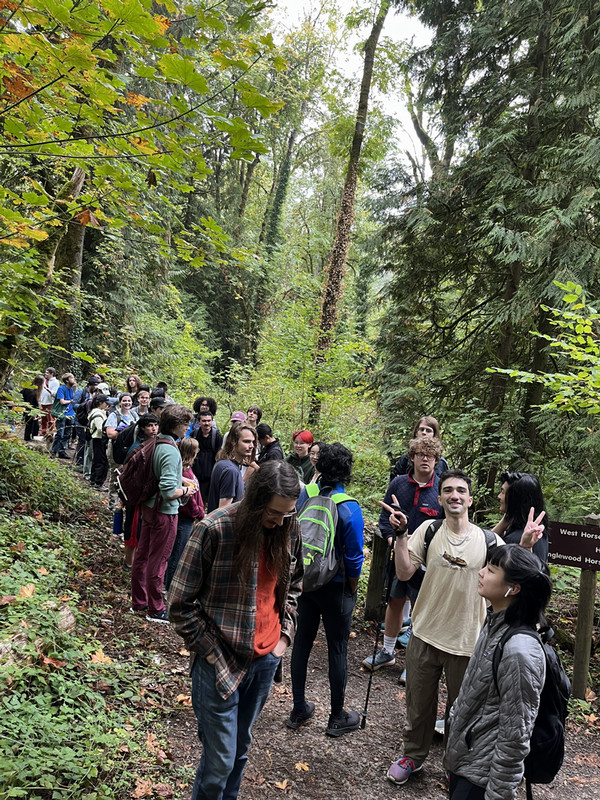 A group of students hiking through a forest, one of whom is flashing peace signs