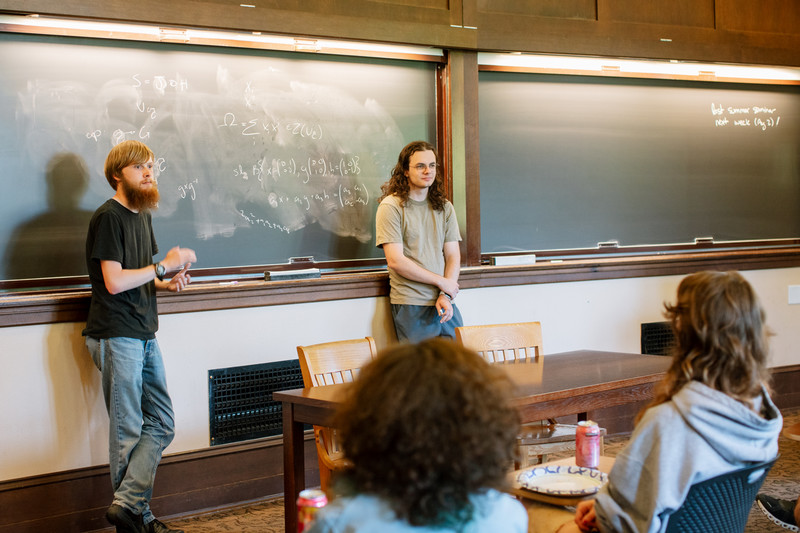 Two physics students stand in front of a chalkboard during a presentation