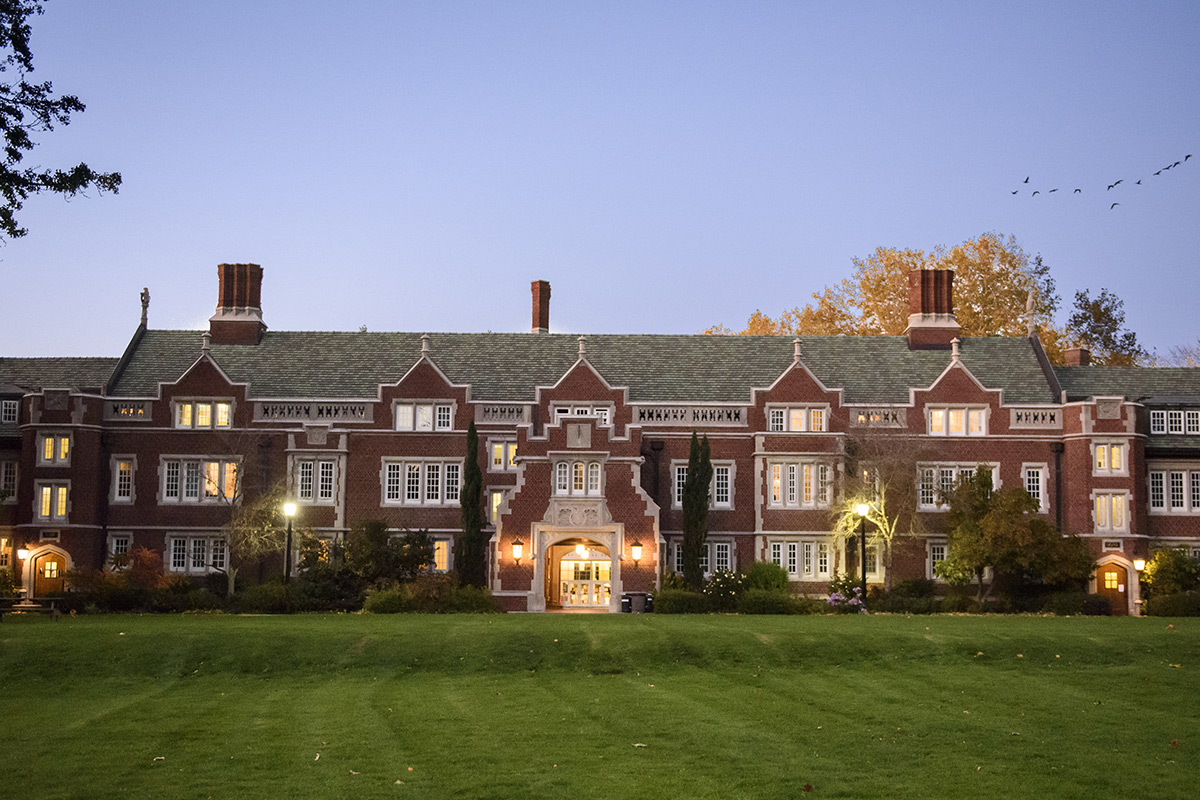 Old Dorm Block at sunset with a flock of birds flying over campus in the distance.