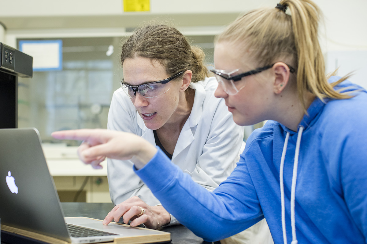 Professor and student looking at and discussing the content displayed on a laptop screen in a science labratory.