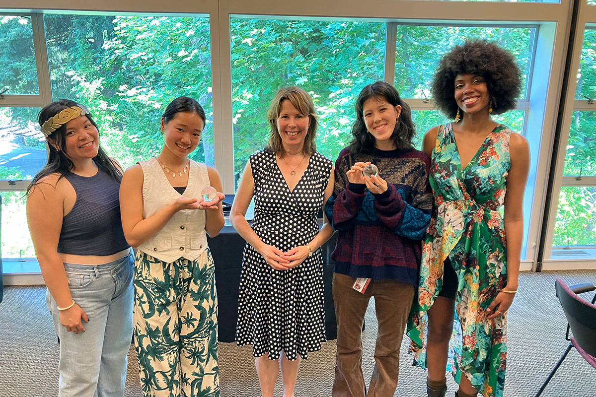 Four students pose stand smiling in a line with President Audrey Bilger in the middle. 