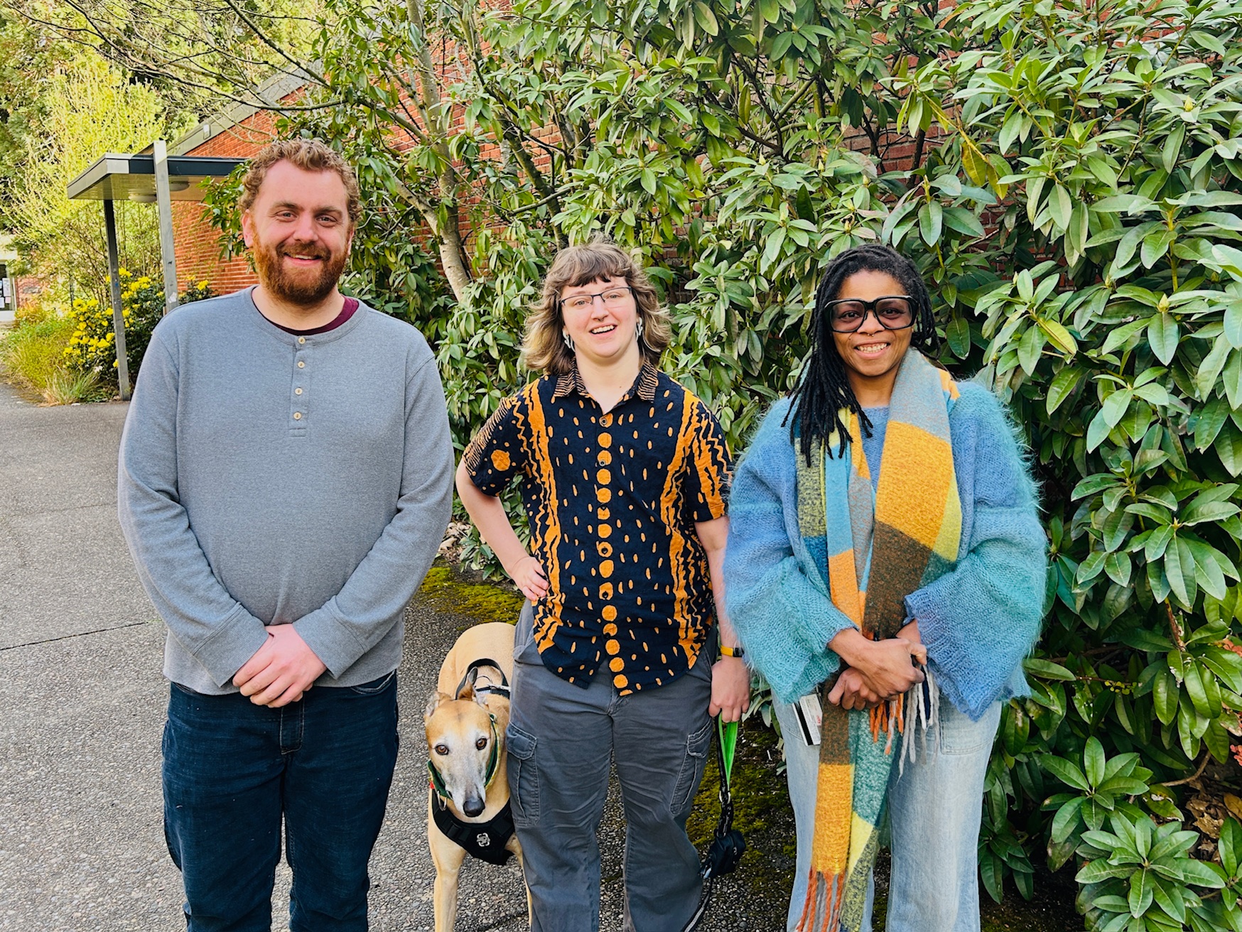 A photo portrait of three IT staff members standing outside with a dog.