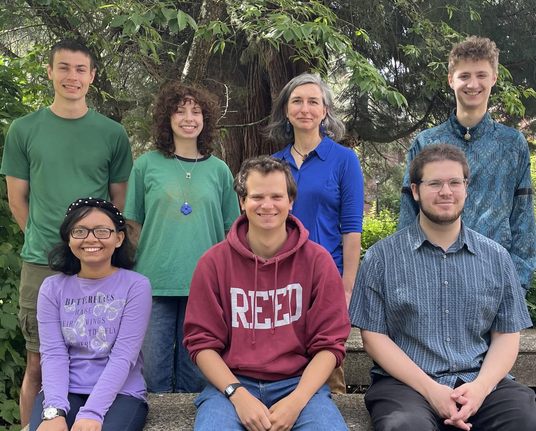 The summer research team outdoors on the Reed campus, standing behind and sitting on a bench.
