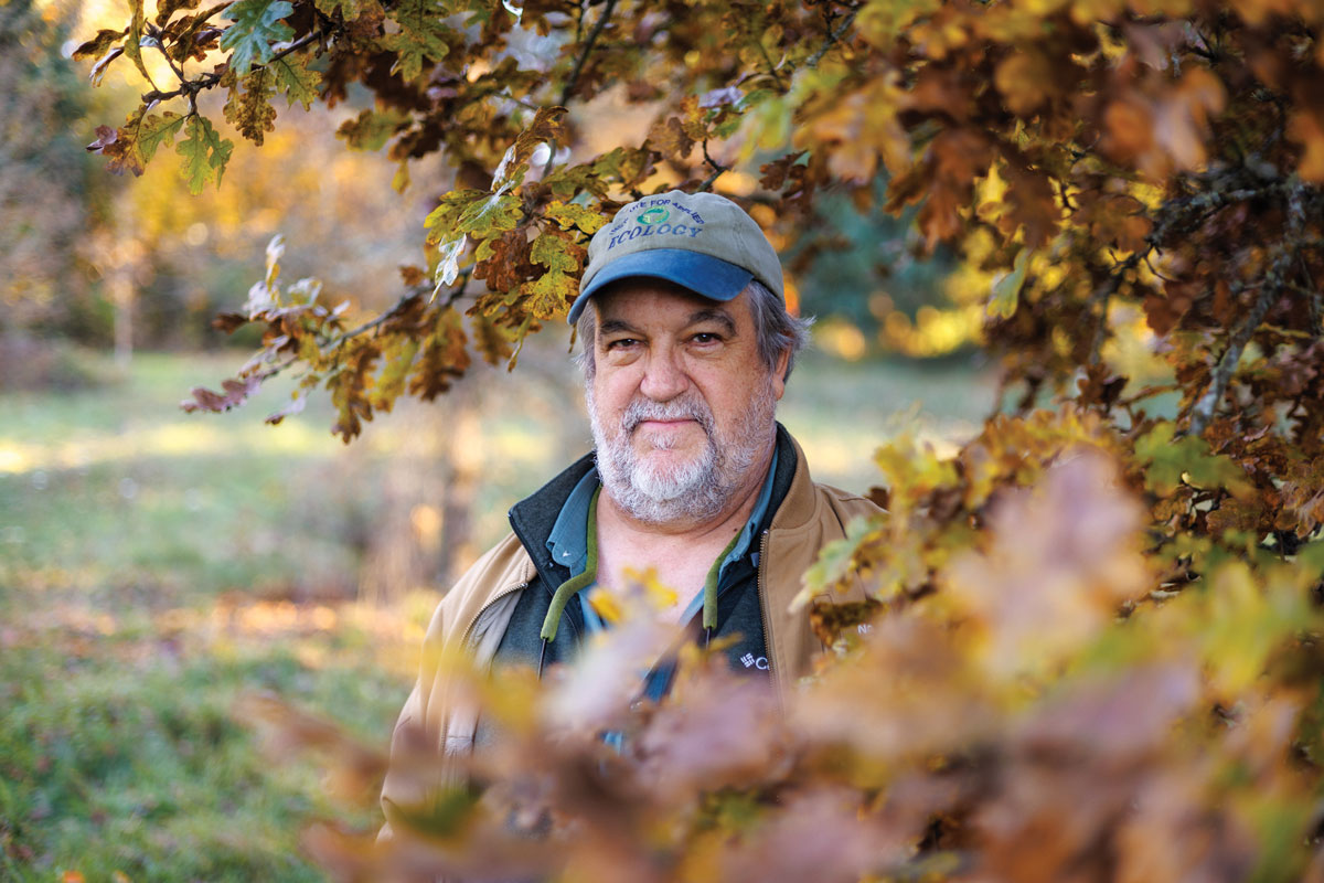 Prof. Keith Karoly standing outdoors, surrounded by rust-colored oak leaves.