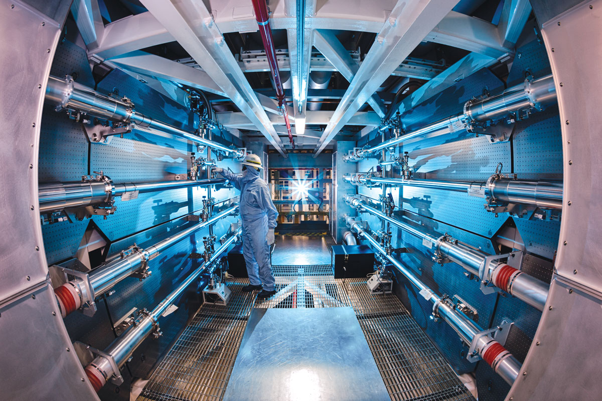 A person in blue protective gear fiddles with something inside the National Ignition Facility at Lawrence Livermore National Laboratory.