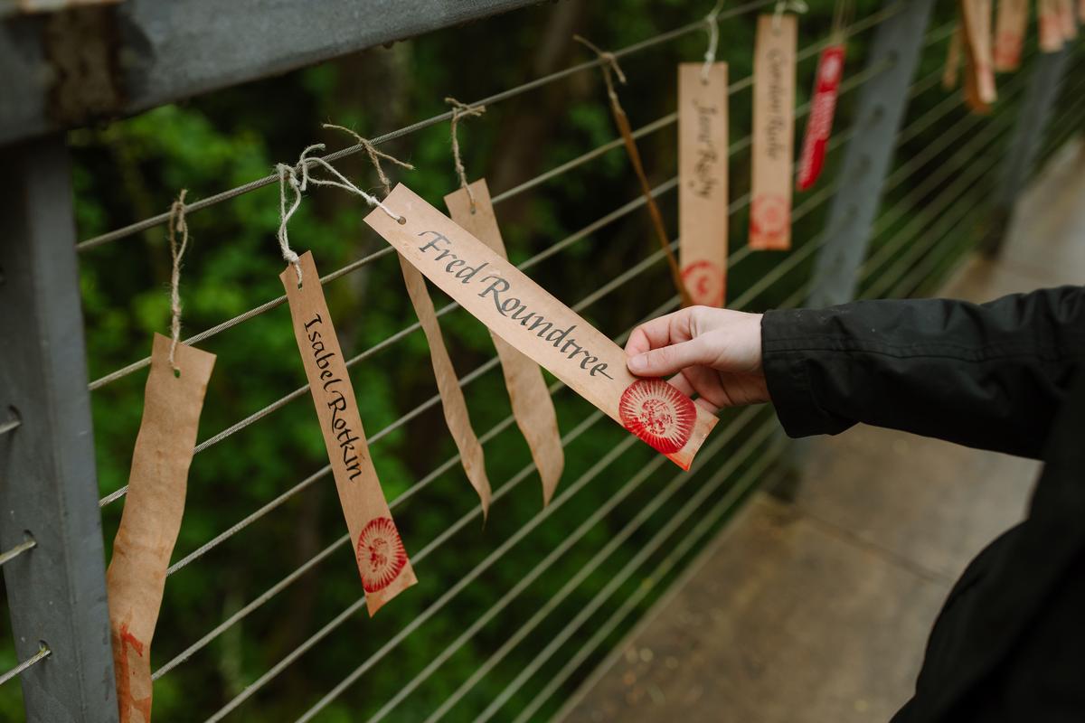 Weathergrams hanging on bridge railing and woman's hand tying more on with twine.