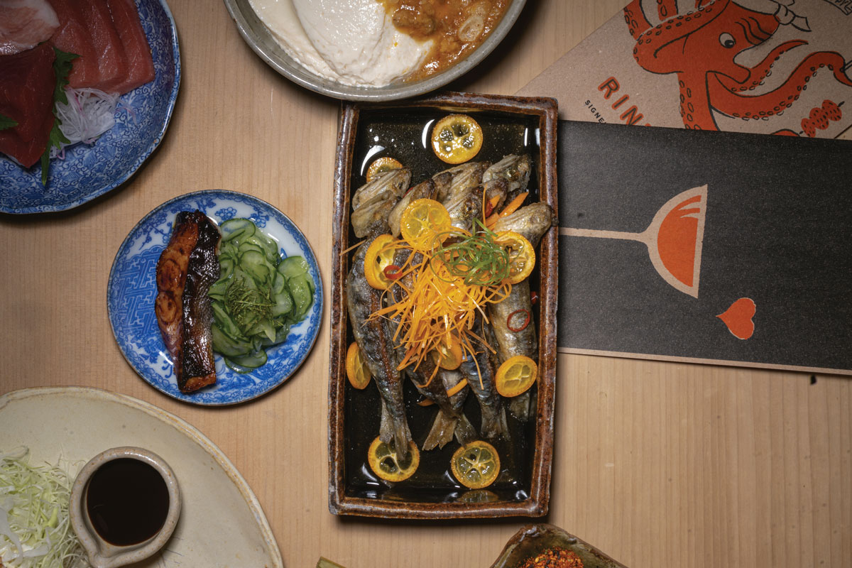 table full of small plates with various cuts of fish with vegetable and fruit garnishes along with menu on the tabletop